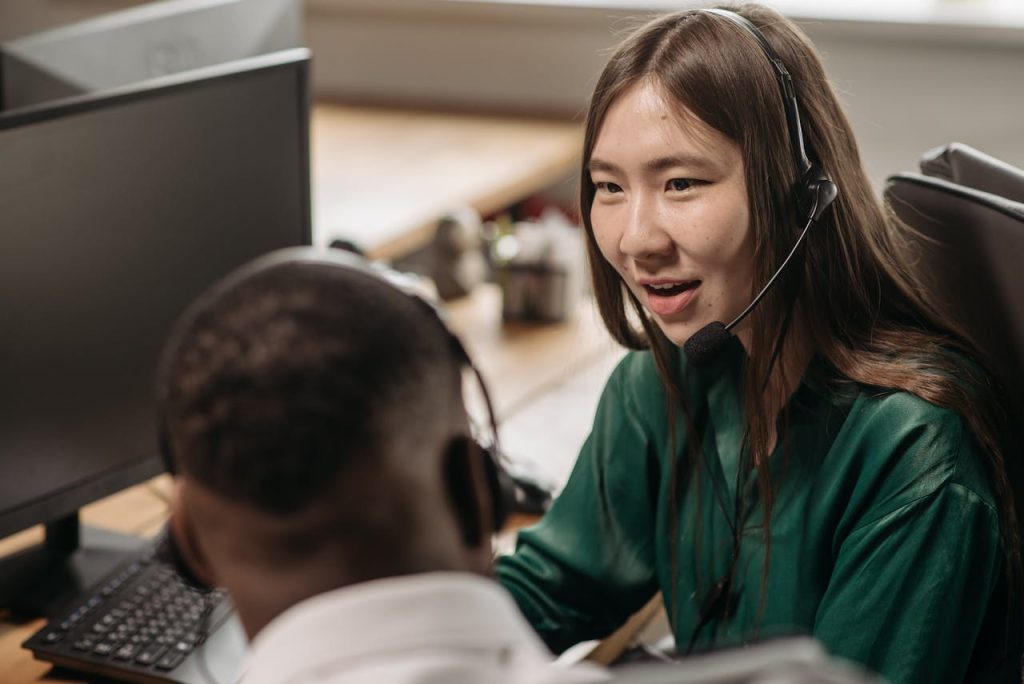 Young Asian woman in a call center talking with a colleague in an office environment.