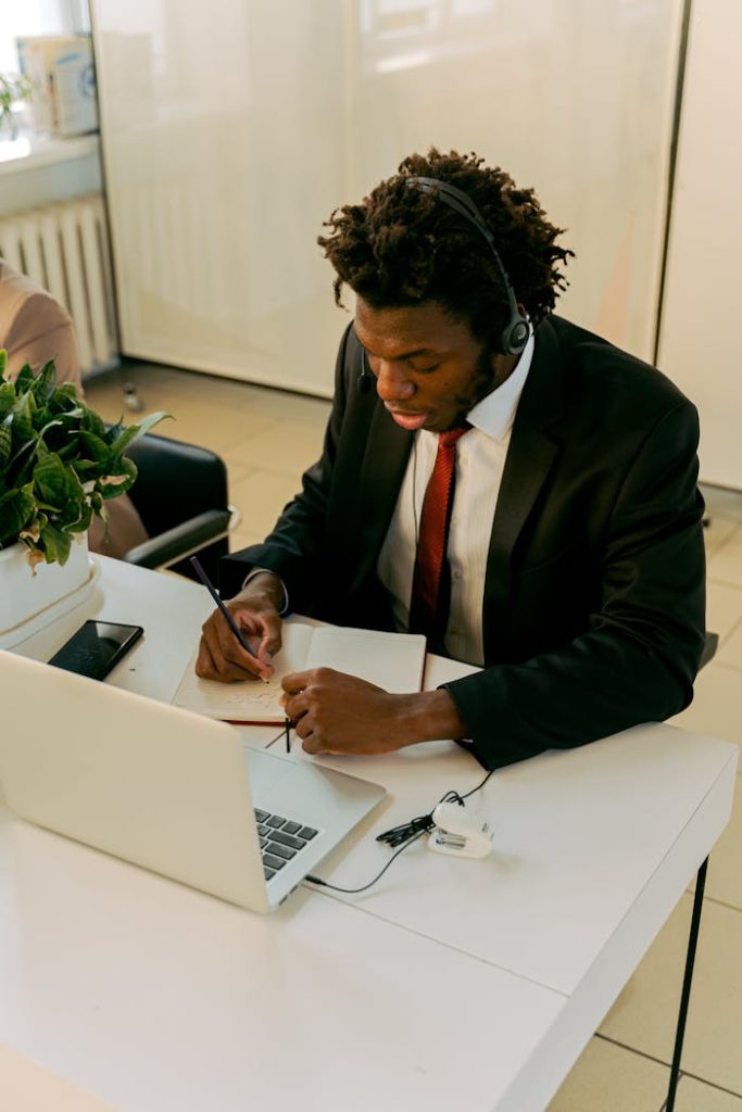 African American businessman with headset writing at a desk in an office environment.