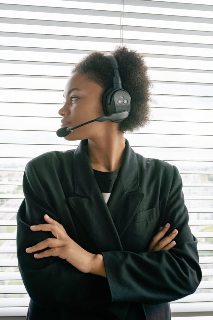African American woman with afro hair wearing a headset and blazer, looking sideways indoors.