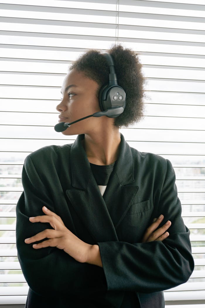 African American woman with afro hair wearing a headset and blazer, looking sideways indoors.